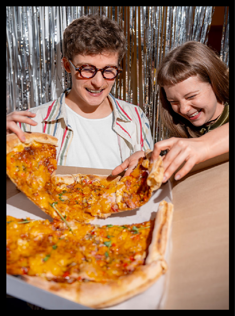 Two friends smiling over a box of pizza