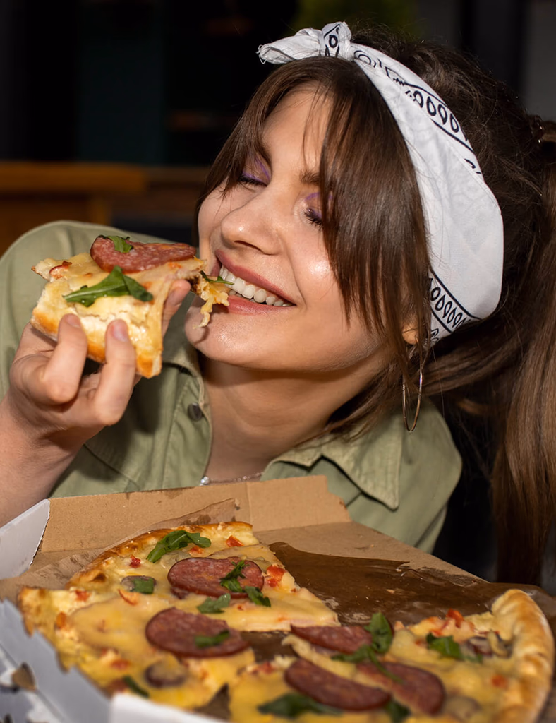 A person smiling while taking a bite of pizza